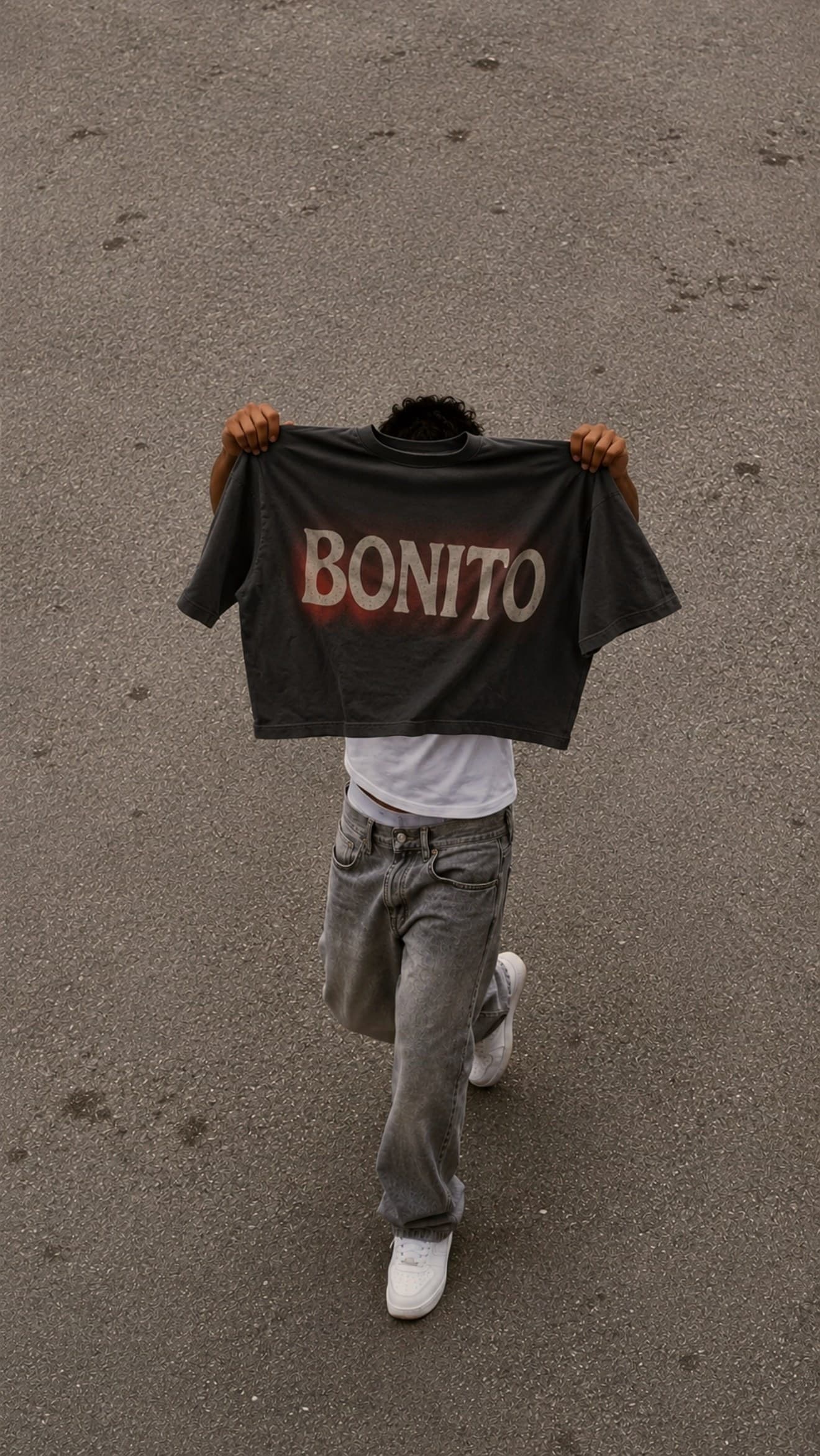 Washed black SOUTELO tee printed with Bonito, held up on asphalt